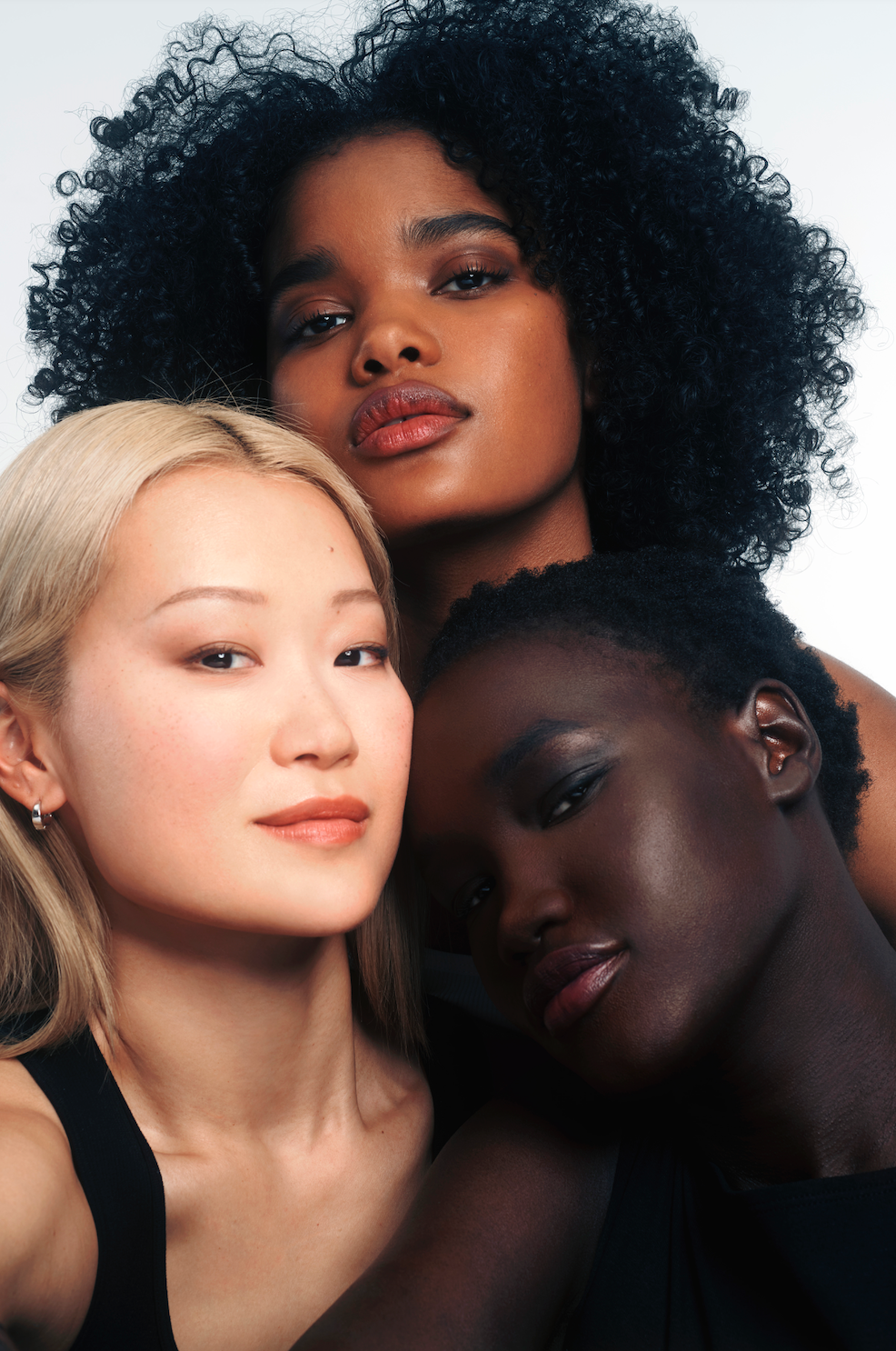 Three women with different hair colors and skin tones posing together.
